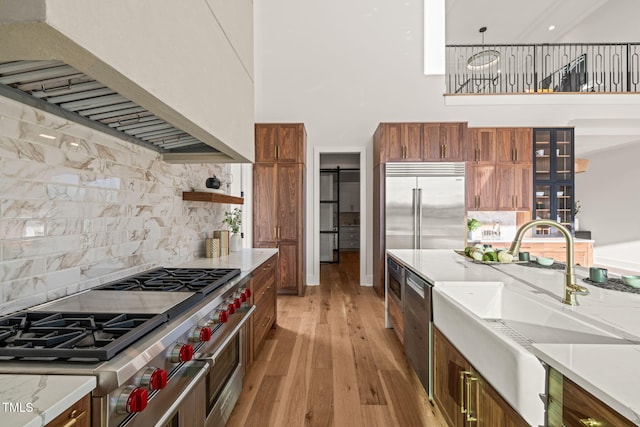 kitchen featuring sink, hanging light fixtures, high quality appliances, light hardwood / wood-style floors, and custom range hood