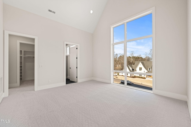 unfurnished bedroom with a walk in closet, light carpet, and high vaulted ceiling