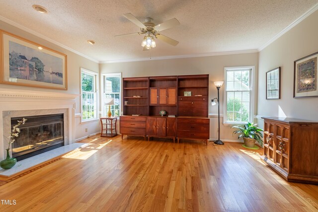 living area with a textured ceiling, light wood-style flooring, a ceiling fan, plenty of natural light, and a high end fireplace