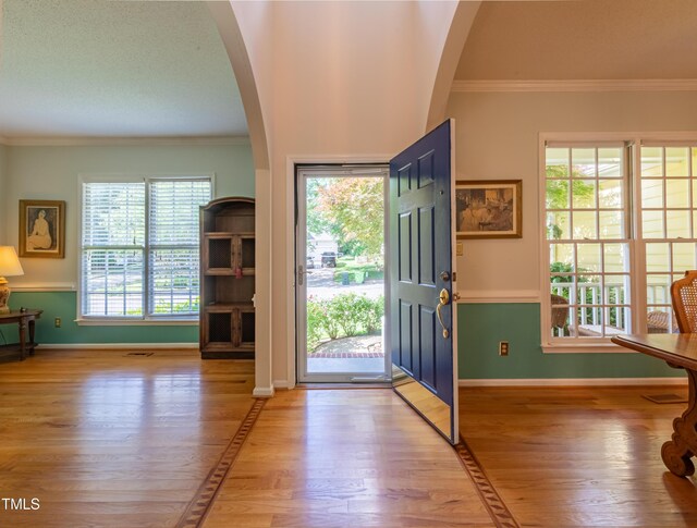 foyer with hardwood / wood-style floors, ornamental molding, arched walkways, and baseboards