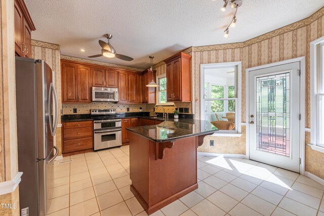 kitchen with appliances with stainless steel finishes, wallpapered walls, a sink, a peninsula, and a kitchen bar