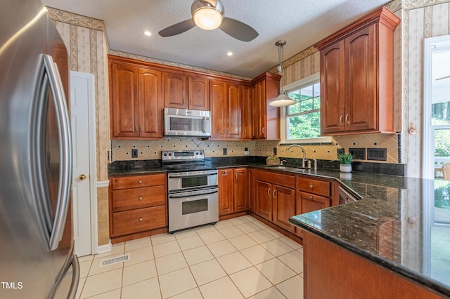 kitchen featuring stainless steel appliances, a sink, wallpapered walls, ceiling fan, and decorative light fixtures