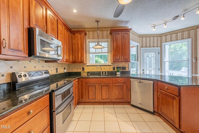 kitchen with stainless steel appliances, wallpapered walls, a sink, a peninsula, and brown cabinets