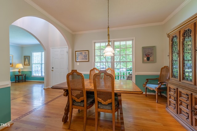 dining area with arched walkways, light wood-style flooring, ornamental molding, and baseboards
