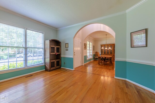 unfurnished room with light wood-type flooring, a chandelier, arched walkways, ornamental molding, and baseboards