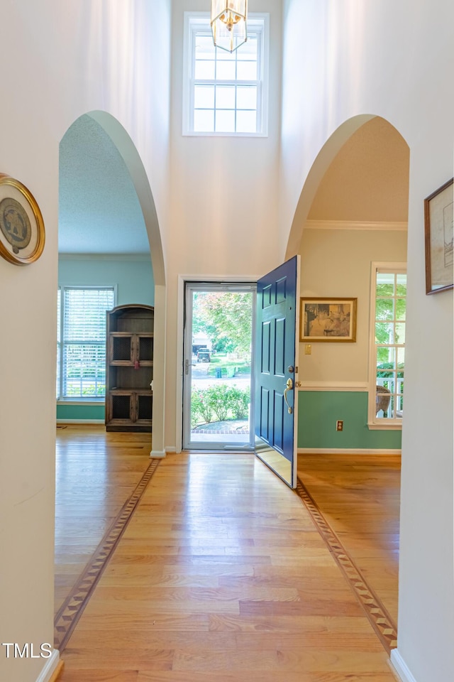foyer with wood finished floors, a towering ceiling, a chandelier, crown molding, and baseboards