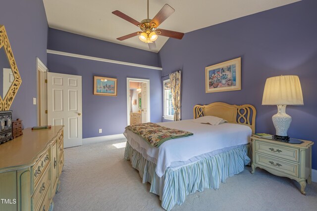 bedroom featuring light carpet, vaulted ceiling, baseboards, ensuite bath, and a ceiling fan