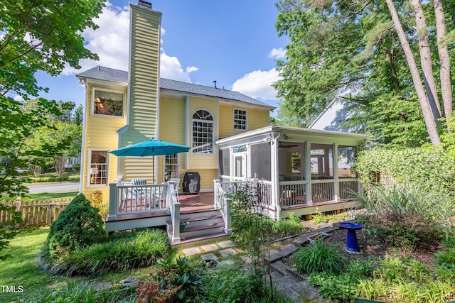 rear view of property featuring a sunroom, a chimney, fence, and a deck