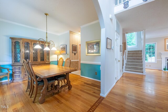 dining space with crown molding, arched walkways, light wood-style flooring, stairway, and baseboards