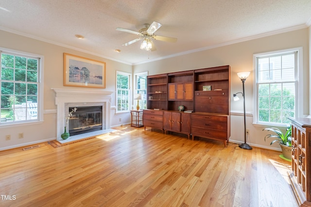 living area with a ceiling fan, light wood finished floors, a glass covered fireplace, crown molding, and baseboards