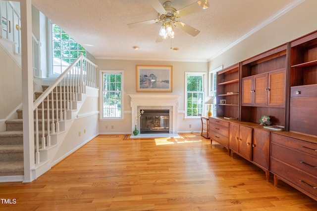 living area with stairway, crown molding, light wood-type flooring, healthy amount of natural light, and a textured ceiling