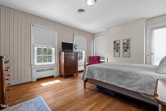 bedroom with a baseboard heating unit, light hardwood / wood-style flooring, and radiator heating unit