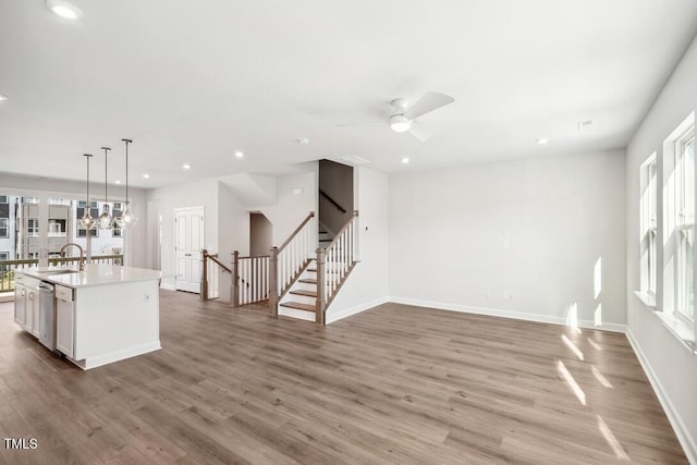 kitchen with stainless steel dishwasher, sink, decorative light fixtures, a center island with sink, and hardwood / wood-style floors