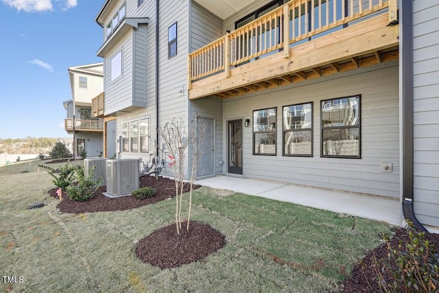 view of exterior entry with a lawn, a balcony, and central AC unit