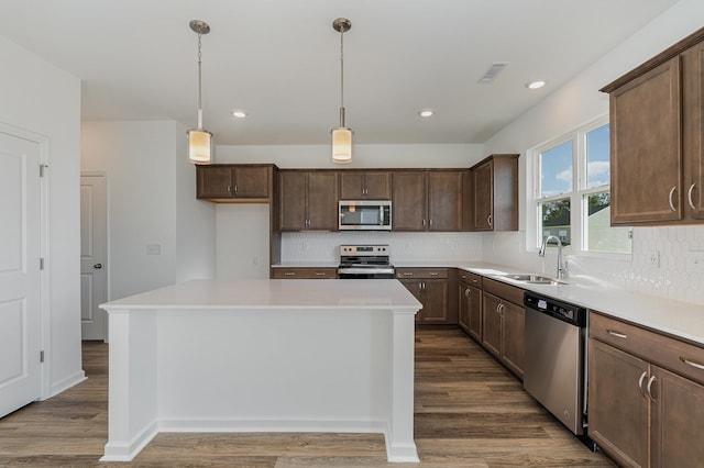 kitchen featuring appliances with stainless steel finishes, hanging light fixtures, a kitchen island, dark hardwood / wood-style floors, and sink