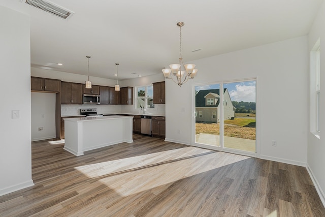 kitchen with pendant lighting, stainless steel appliances, a center island, an inviting chandelier, and hardwood / wood-style floors