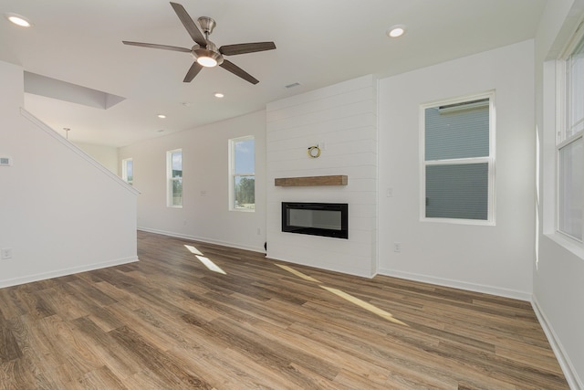 unfurnished living room featuring a large fireplace, ceiling fan, and wood-type flooring