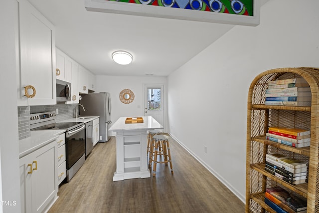 kitchen featuring a center island, white cabinets, hardwood / wood-style flooring, appliances with stainless steel finishes, and a breakfast bar area