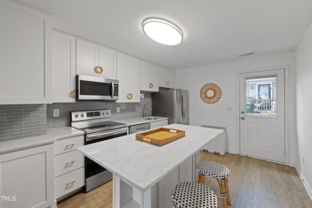 kitchen with white cabinetry, a kitchen island, light wood-type flooring, and appliances with stainless steel finishes