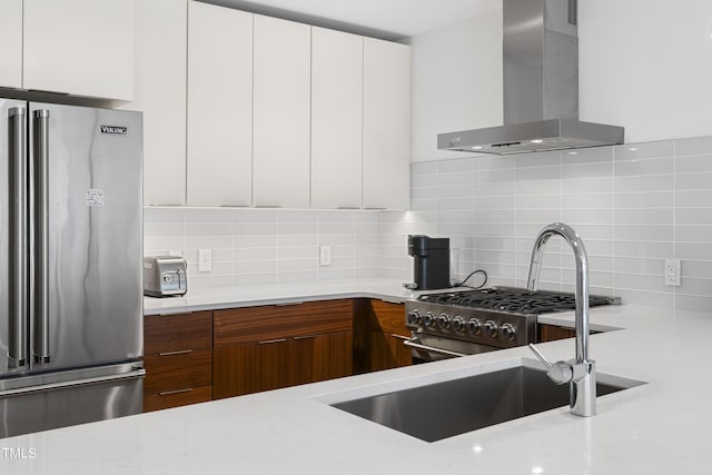 kitchen with white cabinetry, high end appliances, wall chimney range hood, and tasteful backsplash