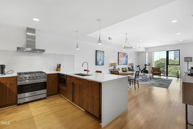 kitchen with kitchen peninsula, light wood-type flooring, stainless steel appliances, sink, and wall chimney range hood