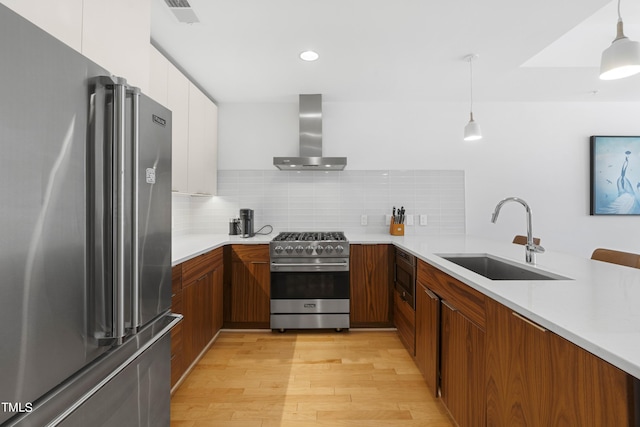 kitchen featuring premium appliances, sink, wall chimney range hood, decorative light fixtures, and white cabinetry