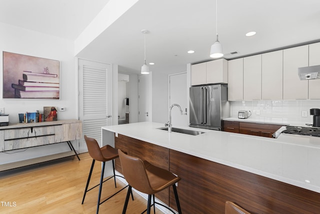 kitchen with sink, a kitchen breakfast bar, decorative light fixtures, high quality fridge, and white cabinets