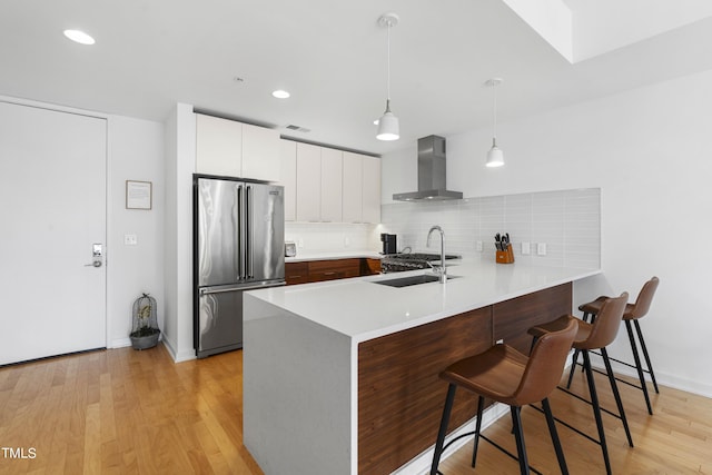 kitchen featuring a breakfast bar, wall chimney exhaust hood, kitchen peninsula, high end fridge, and light wood-type flooring