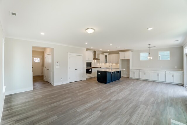 2023 Seneca Dr Lot 32, Raleigh, NC 27604 - kitchen with light hardwood / wood-style flooring, a center island with sink, hanging light fixtures, wall chimney exhaust hood, and white cabinets