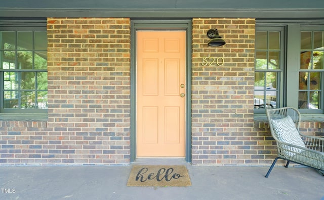 view of exterior entry with brick siding and a porch