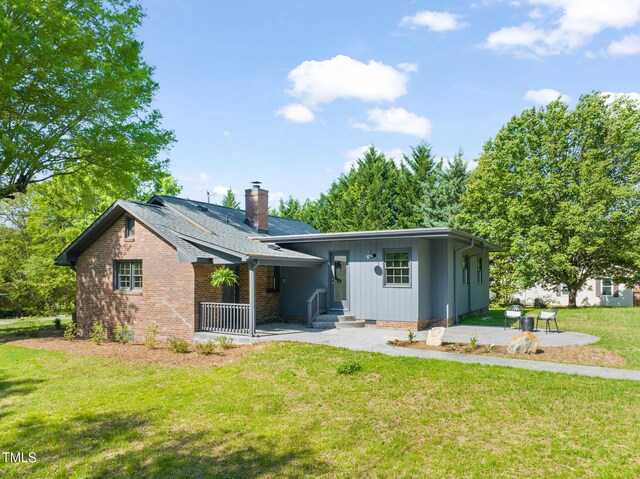 rear view of property featuring a chimney, brick siding, a patio area, a lawn, and board and batten siding
