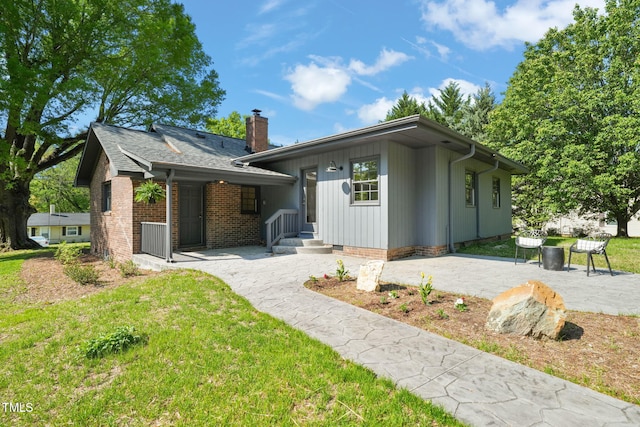 view of front of property with a front lawn, a patio area, brick siding, and a chimney