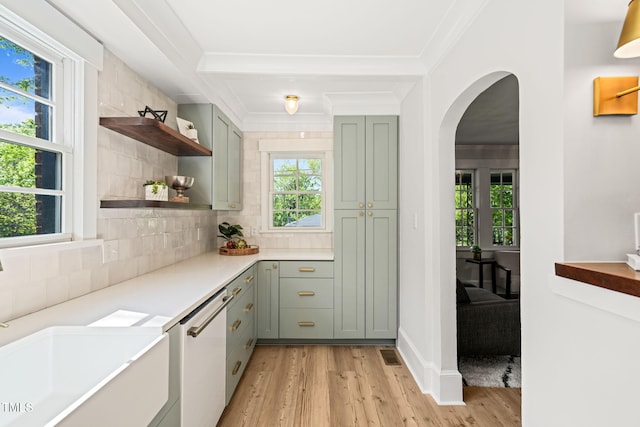 bar featuring a sink, dishwasher, arched walkways, light wood-style flooring, and backsplash