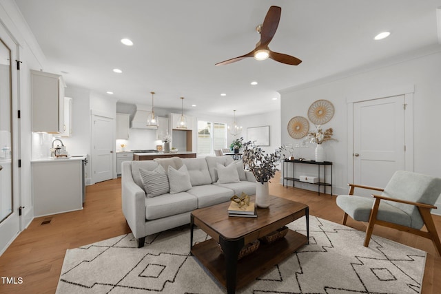 living room featuring ceiling fan with notable chandelier, light hardwood / wood-style flooring, and ornamental molding