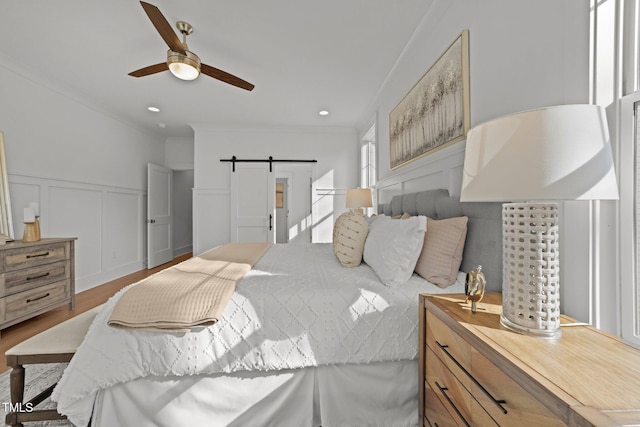 bedroom featuring ceiling fan, a barn door, light wood-type flooring, and crown molding