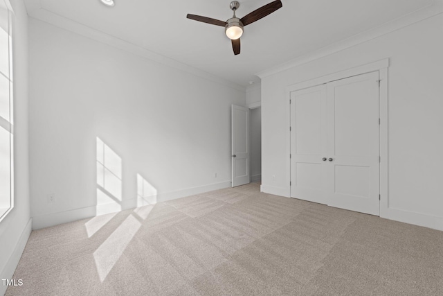 unfurnished bedroom featuring crown molding, ceiling fan, a closet, and light carpet