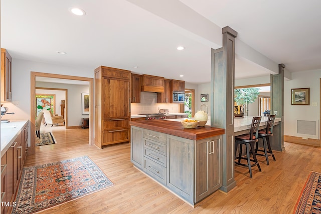 kitchen featuring butcher block countertops, light hardwood / wood-style flooring, range, tasteful backsplash, and built in microwave