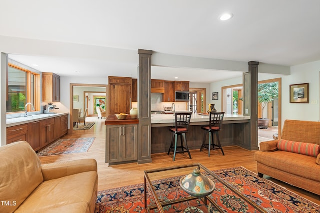 living room featuring light wood-type flooring, plenty of natural light, and ornate columns