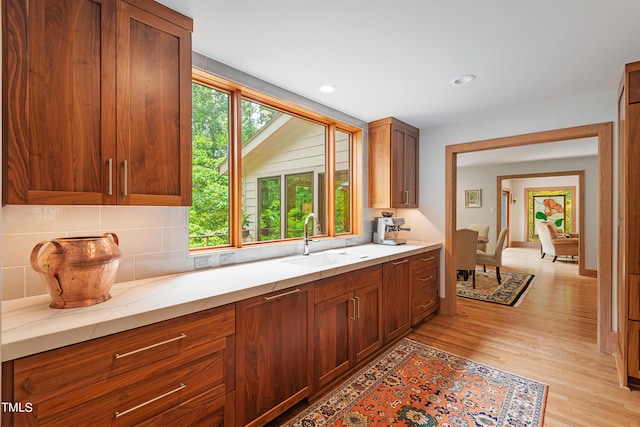 kitchen with light stone countertops, sink, decorative backsplash, and light hardwood / wood-style flooring