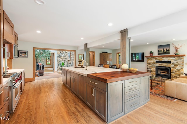 kitchen featuring decorative columns, high end stainless steel range, an island with sink, a stone fireplace, and light wood-type flooring