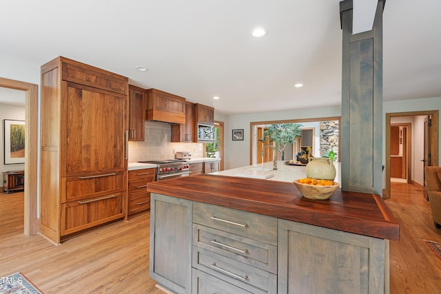 kitchen with sink, wooden counters, light wood-type flooring, a kitchen island with sink, and decorative backsplash