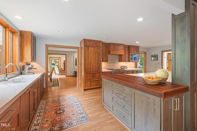 kitchen with sink, backsplash, wooden counters, high end range, and light hardwood / wood-style floors