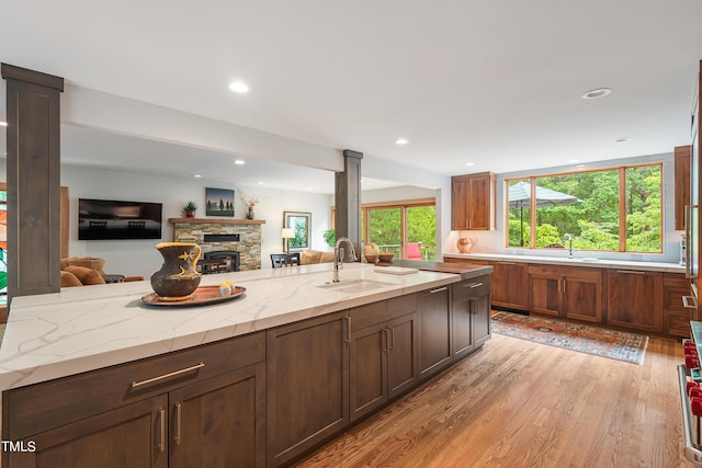 kitchen featuring light stone countertops, sink, a stone fireplace, and light wood-type flooring