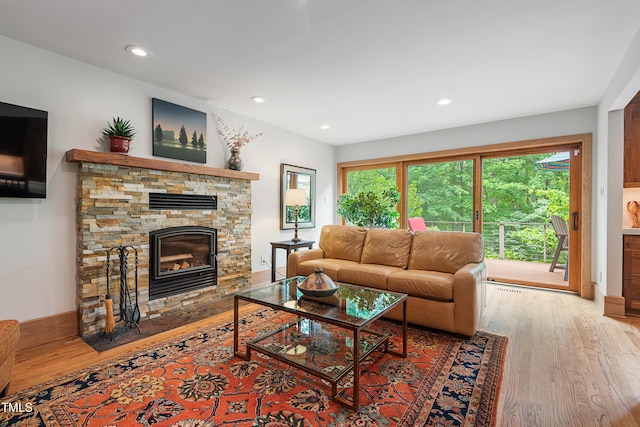 living room featuring wood-type flooring, a stone fireplace, and a healthy amount of sunlight