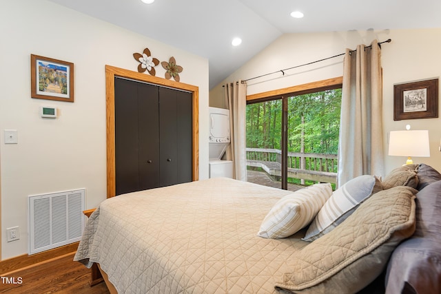 bedroom featuring dark wood-type flooring, stacked washer / drying machine, vaulted ceiling, and a closet