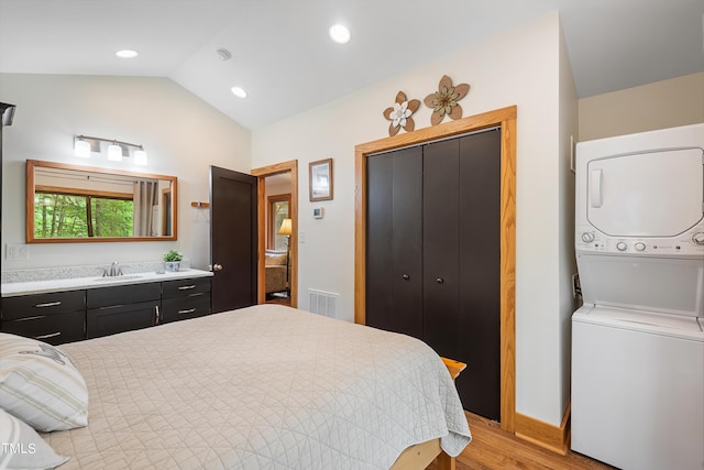 bedroom featuring stacked washer and dryer, sink, light hardwood / wood-style floors, vaulted ceiling, and a closet