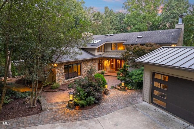 view of front facade featuring driveway, stone siding, a standing seam roof, metal roof, and a garage