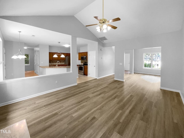 unfurnished living room with hardwood / wood-style floors, high vaulted ceiling, ceiling fan with notable chandelier, and sink