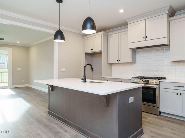 kitchen with pendant lighting, stainless steel range with gas cooktop, sink, an island with sink, and light hardwood / wood-style floors