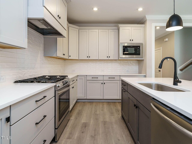 kitchen with light wood-type flooring, stainless steel appliances, sink, decorative light fixtures, and white cabinetry